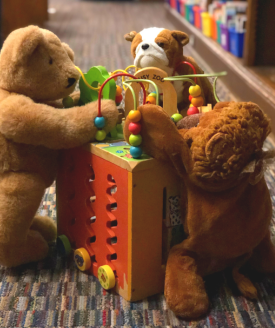 3 stuffed animals "play" with a toy in the library