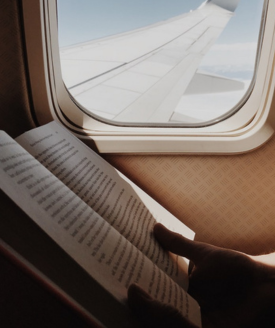 Image of a book next to a plane window. 